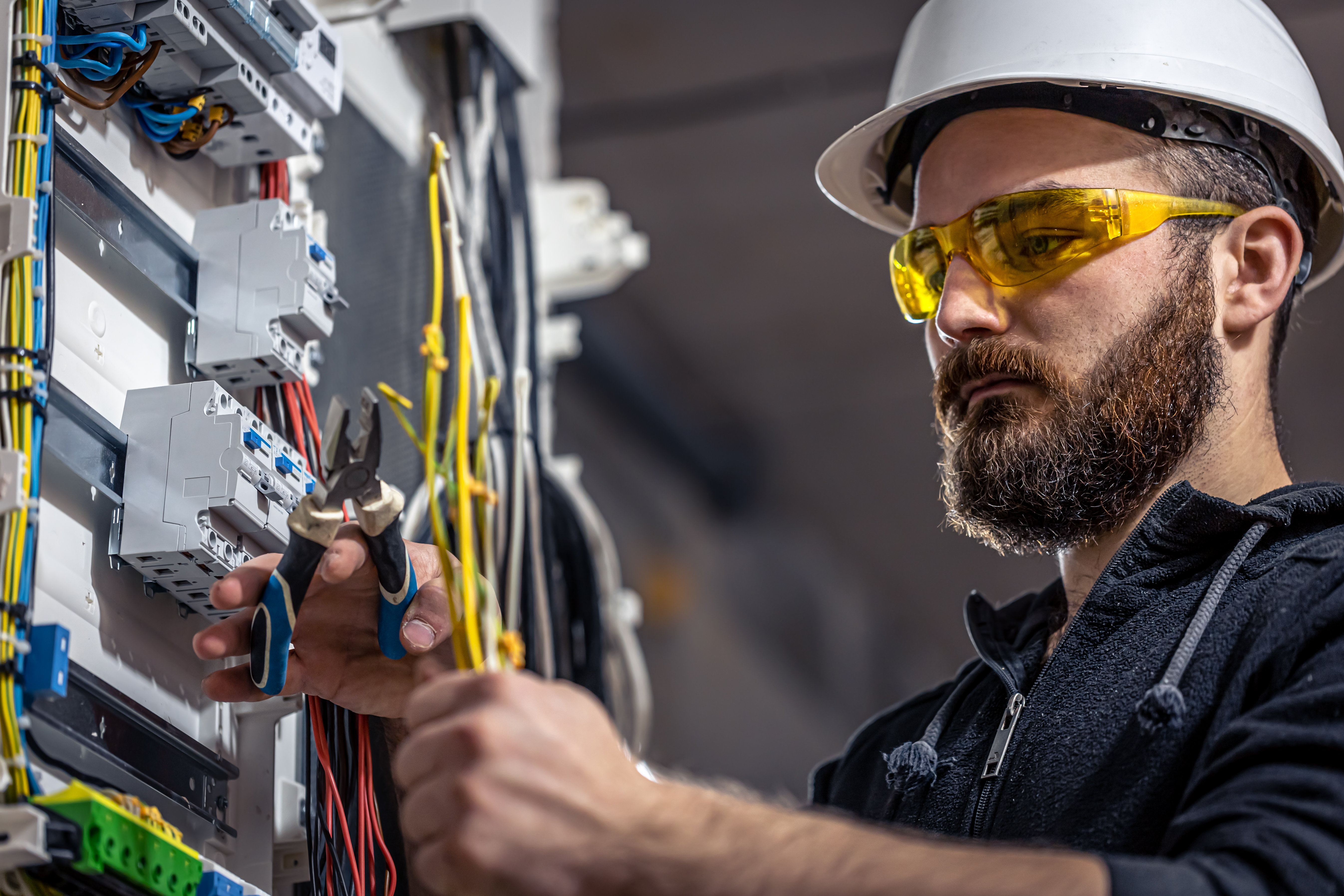 Elektriker arbeider i sikringsskap med vernebriller og hjelm
